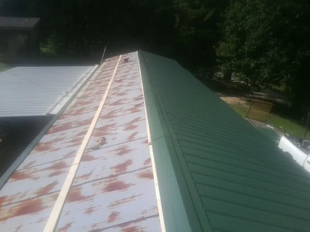 Old rusted panels beside newly installed green metal roofing — Wind Damage Roof Repair by Roofing Brothers in Glen Burnie