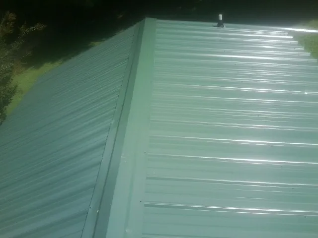 New green metal panels meeting at the ridge of a roof — Flat Roof Repair work by our crew in Glen Burnie