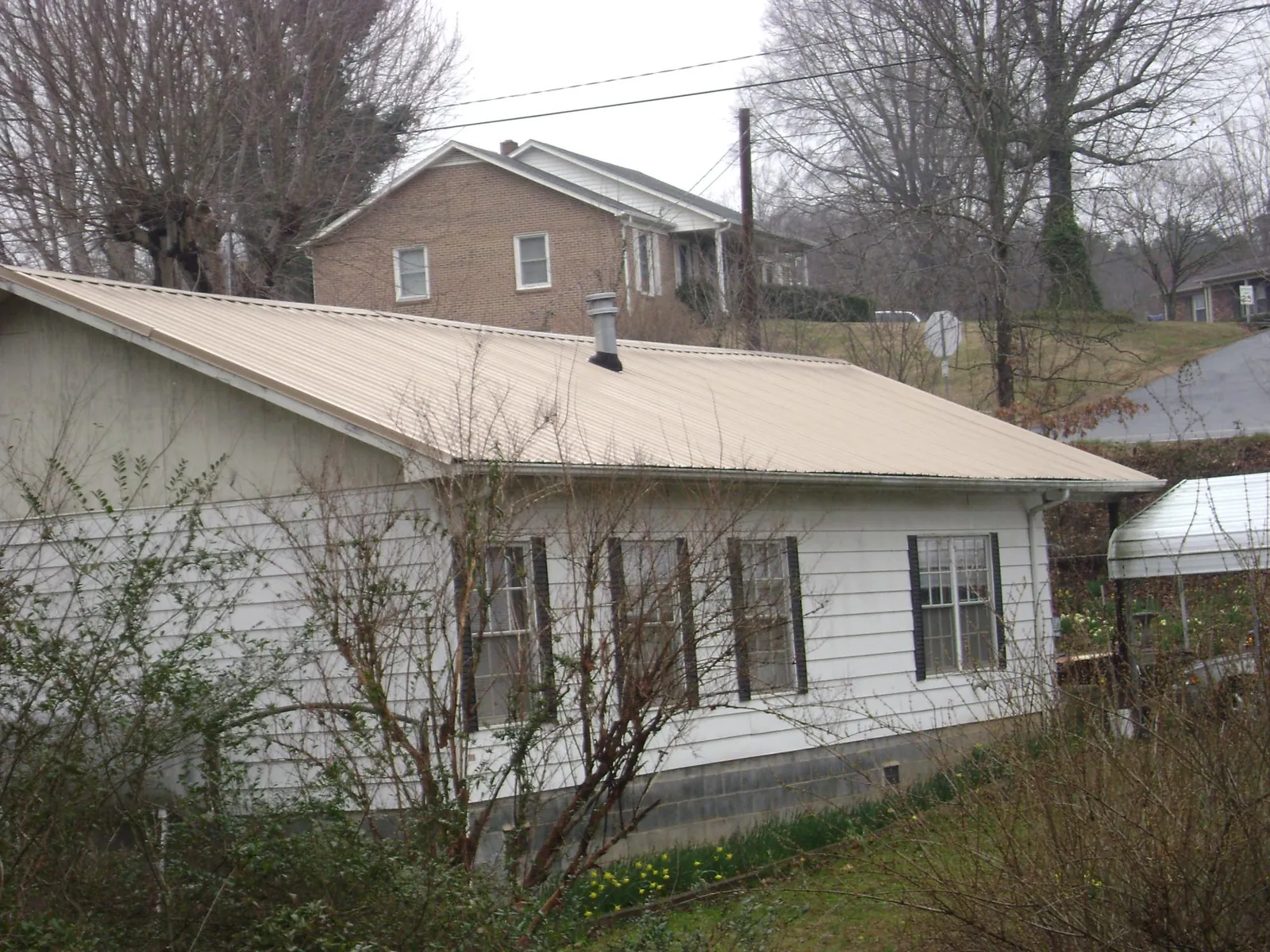 Tan metal roof on a white sided house set into a hillside — Commercial Roofing by Roofing Brothers in Glen Burnie