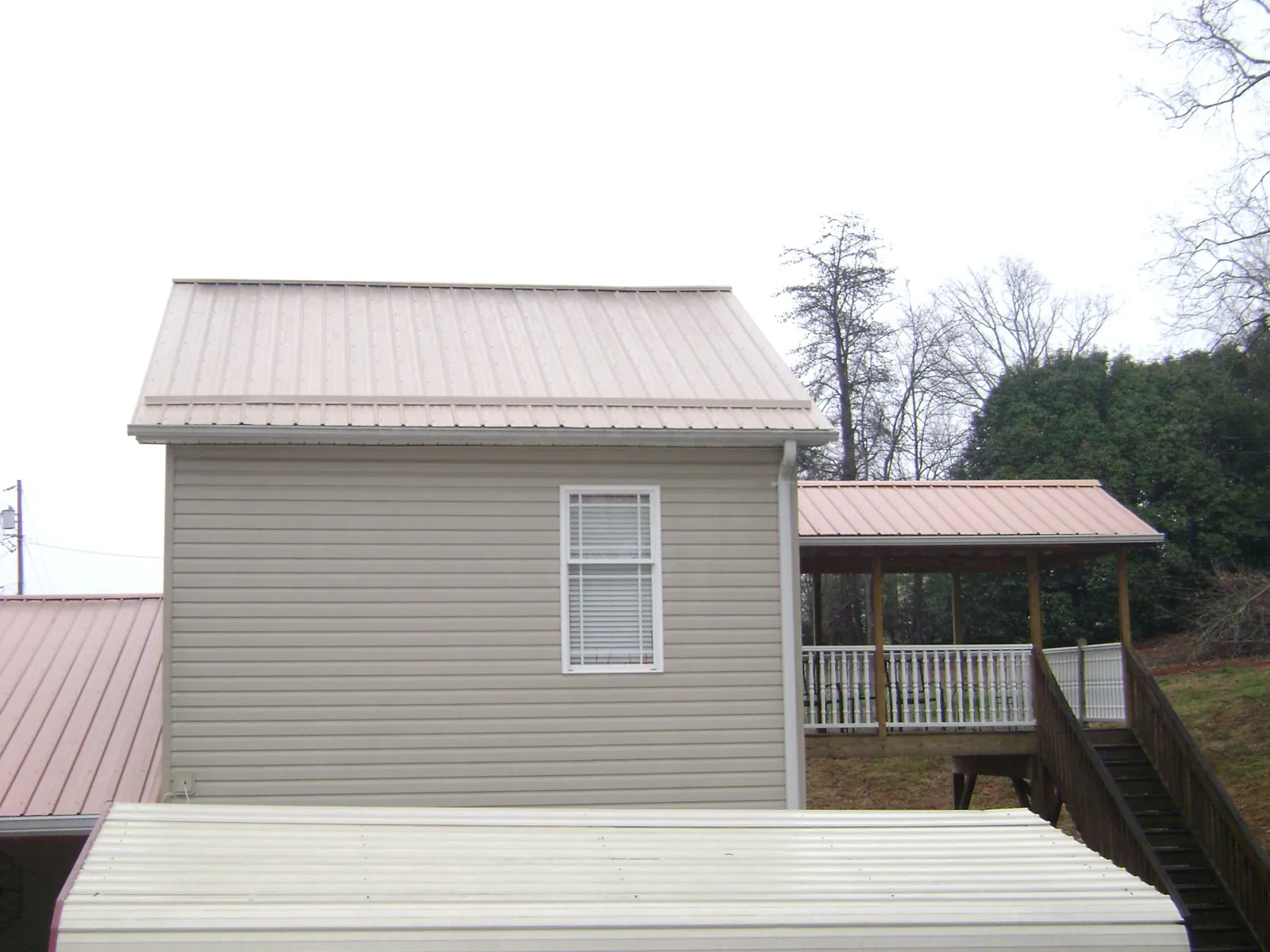 Tan metal roofs on a two story addition and attached porch, from a Roof Replacement job in Glen Burnie